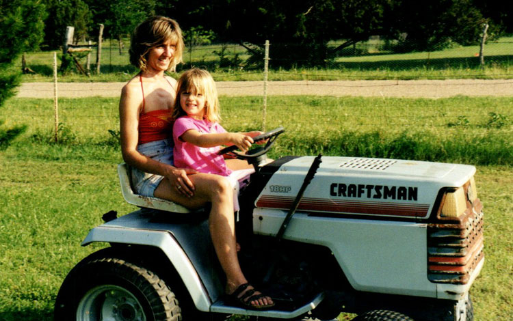 A child and her mom riding on a lawn mower.